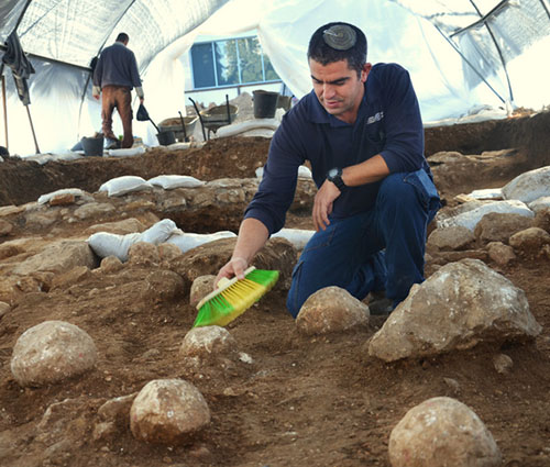 Kfir Arbib, excavation director on behalf of the Israel Antiquities Authority, cleans one of the sling stones. Photographic credit: Yoli Shwartz, courtesy of the Israel Antiquities Authority.